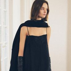 A Zara model walking in a black cape worn like a scarf, a black spaghetti strap maxi dress, and black gloves.
